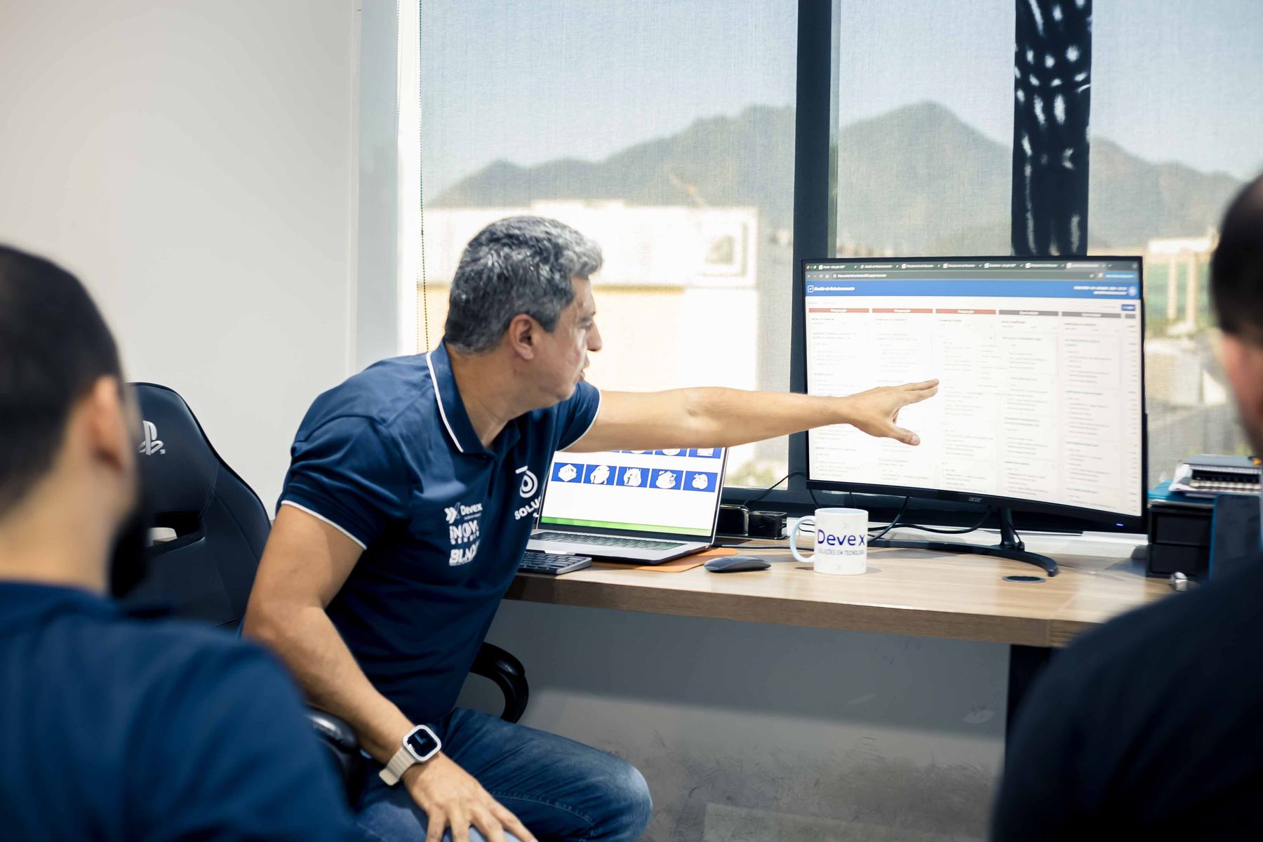 Líder aponta para um painel de indicadores exibido no monitor enquanto conversa com um colega.