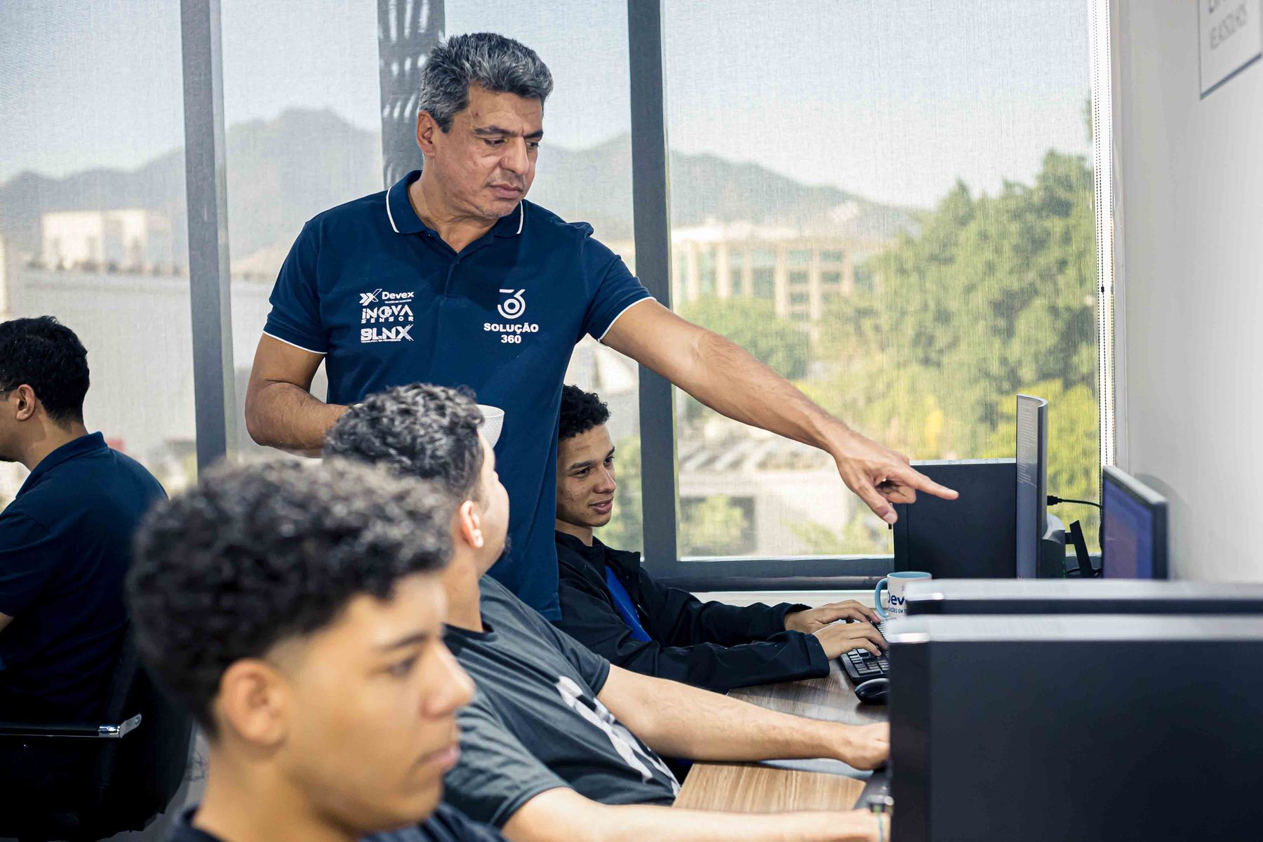 Líder apontando para a tela de um computador enquanto orienta a equipe no escritório
