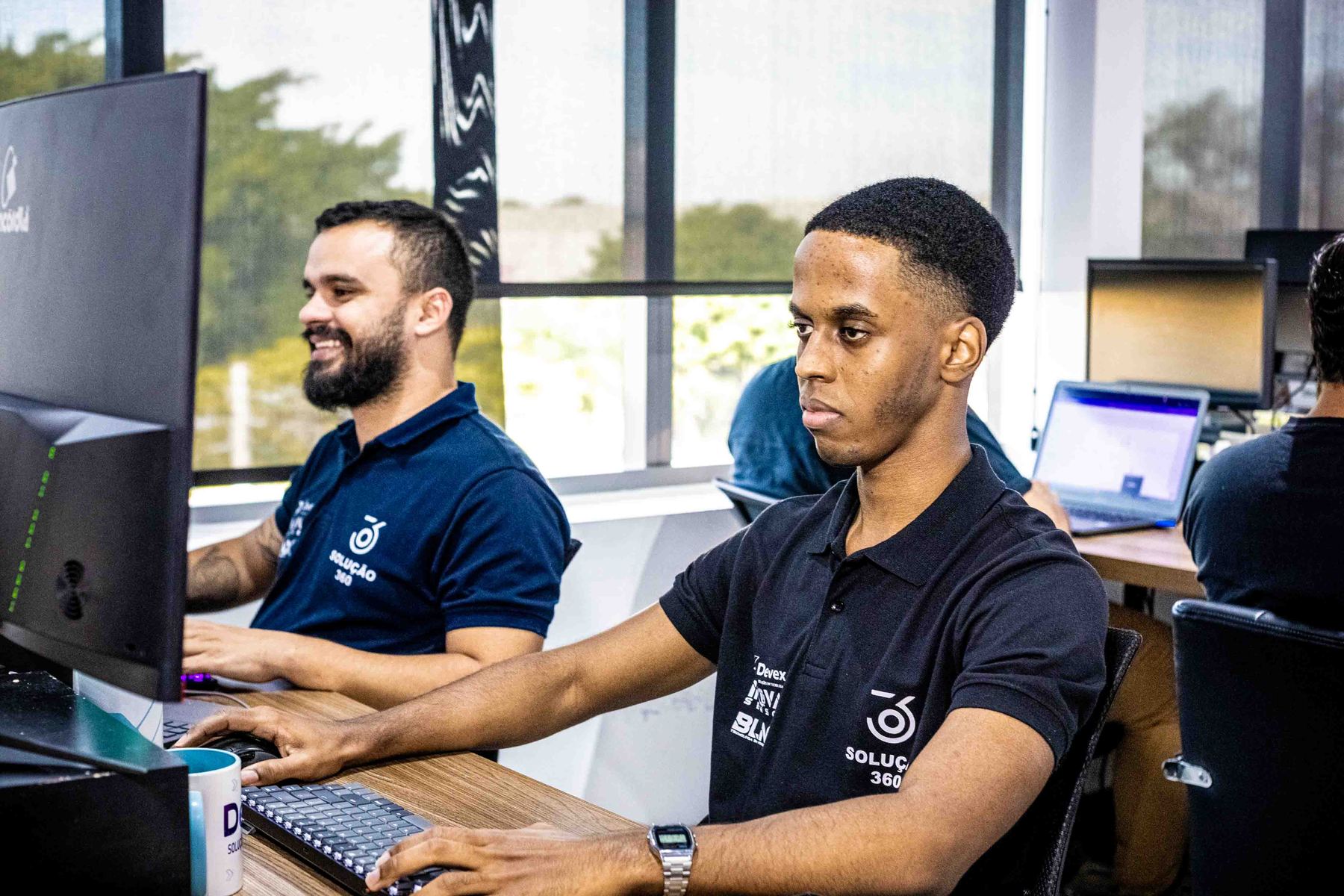 Dois desenvolvedores trabalhando lado a lado em seus computadores no escritório.