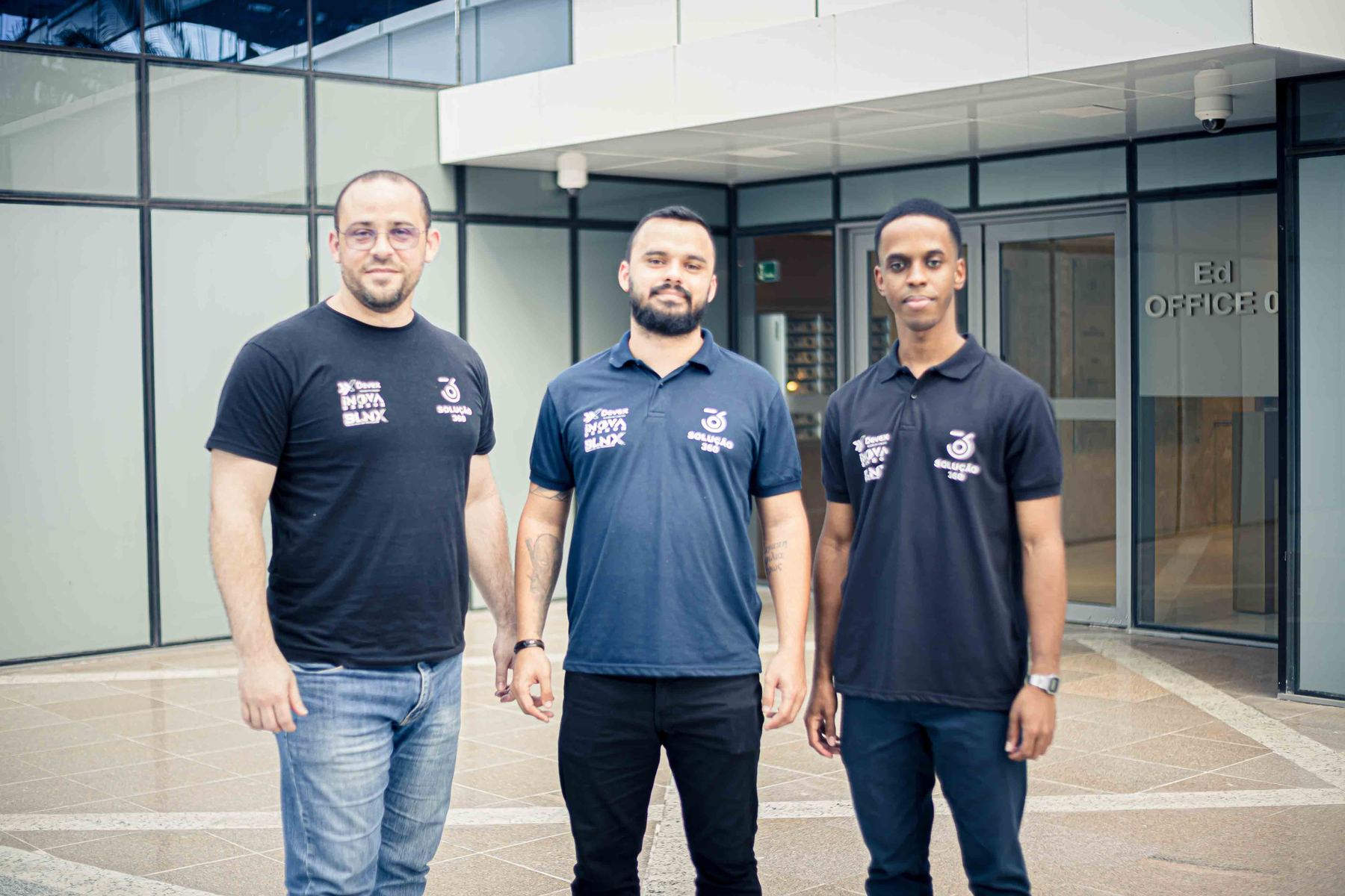Três integrantes do time Devex lado a lado no átrio do prédio da empresa